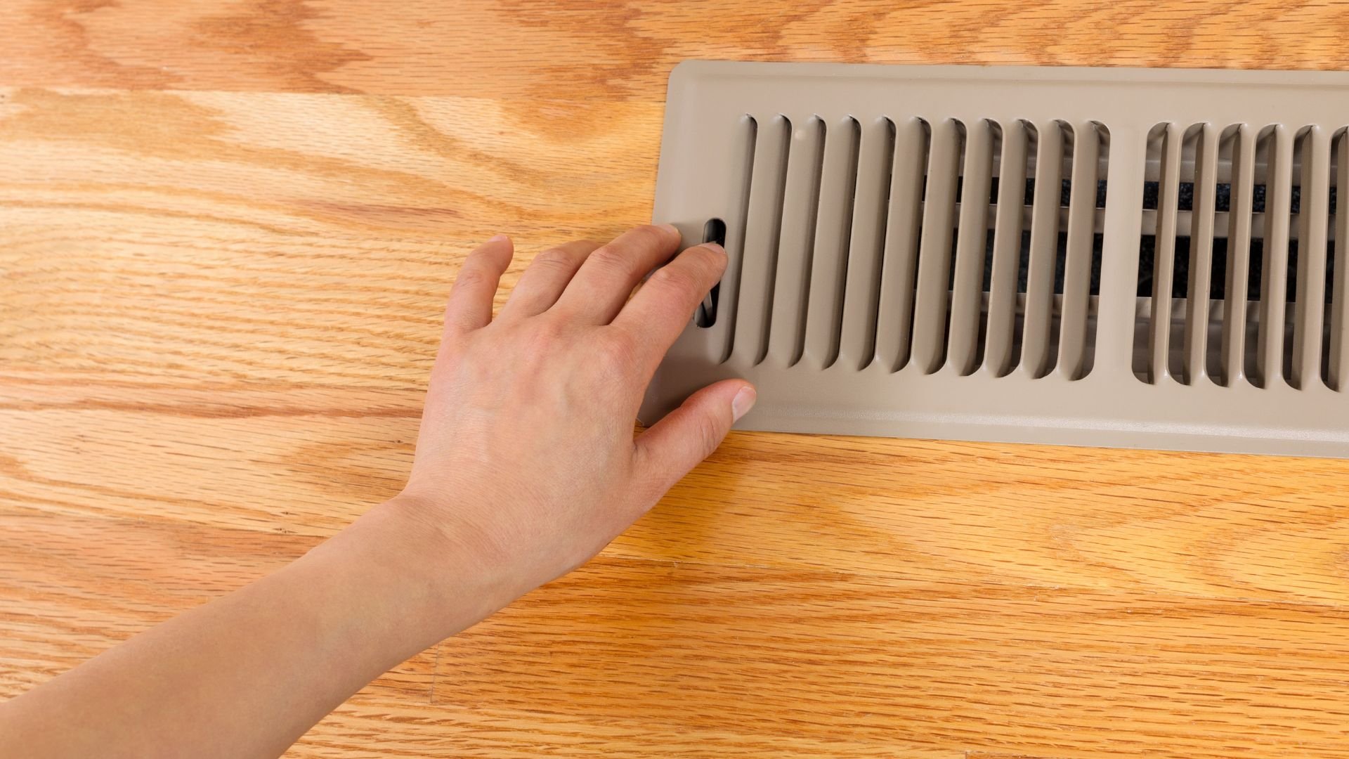 Hand adjusting wall vent on wooden floor heating or air conditioning