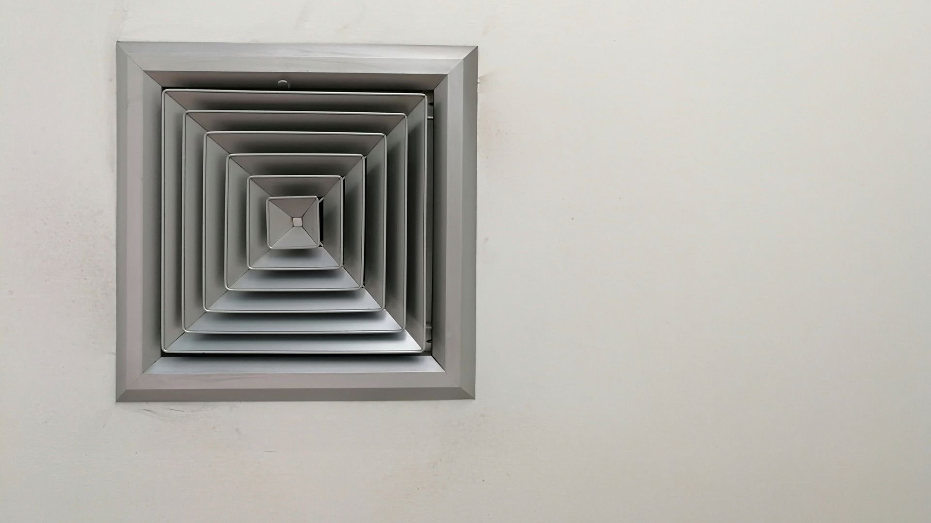 Square air vent with concentric layers mounted on a plain white wall